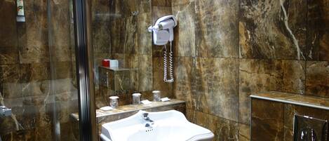Un baño con pared de mármol, un lavamanos, un perchero para toallas y una ducha.