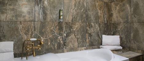 A bathroom with a marble wall, a freestanding bathtub, and a towel rack.