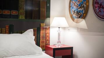 Une chambre d’hôtel comprenant un lit, une table de chevet avec une lampe, une bibliothèque remplie de livres et une peinture décorative au plafond.