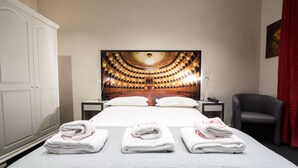 Habitación de hotel con una cama grande, un cuadro en la pared, una silla y un escritorio con una lámpara.