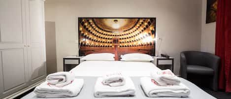 Habitación de hotel con una cama grande, un cuadro en la pared, una silla y un escritorio con una lámpara.