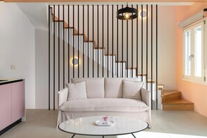 Un salon moderne comprenant un canapé, une table basse en verre, un escalier avec des marches en bois et un mur orné de lignes verticales.