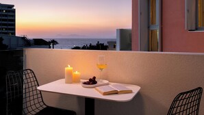 A balcony with a table, two candles, a glass of wine, a bowl of fruit, and an open book. - Iviskos - Island View (Ιαλυσός)