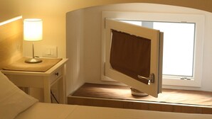 Une chambre d’hôtel avec un lit, une table de chevet avec une lampe, une fenêtre avec des rideaux et une petite table avec une télécommande.