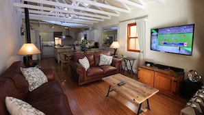 A living room with a brown leather sofa, a wooden coffee table, and a television displaying a sports game. - LeBonheur (Cape Town)