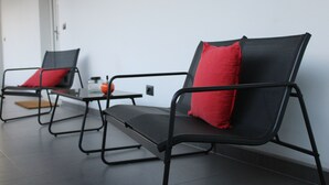 Une pièce moderne avec deux chaises noires dotées de coussins rouges, une petite table sur laquelle se trouvent une bouteille et un verre, et une porte visible au fond.