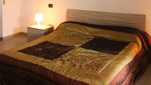 Une chambre avec un plafond en briques, un lit recouvert d’une couvre-lit à motifs, une table de chevet avec une lampe et un tableau encadré accroché au mur.