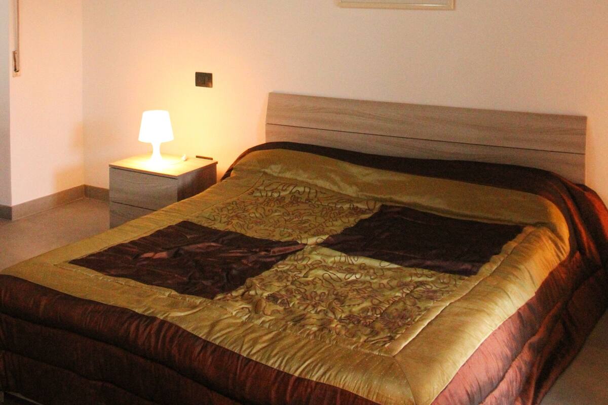 Une chambre avec un plafond en briques, un lit recouvert d’une couvre-lit à motifs, une table de chevet avec une lampe et un tableau encadré accroché au mur.