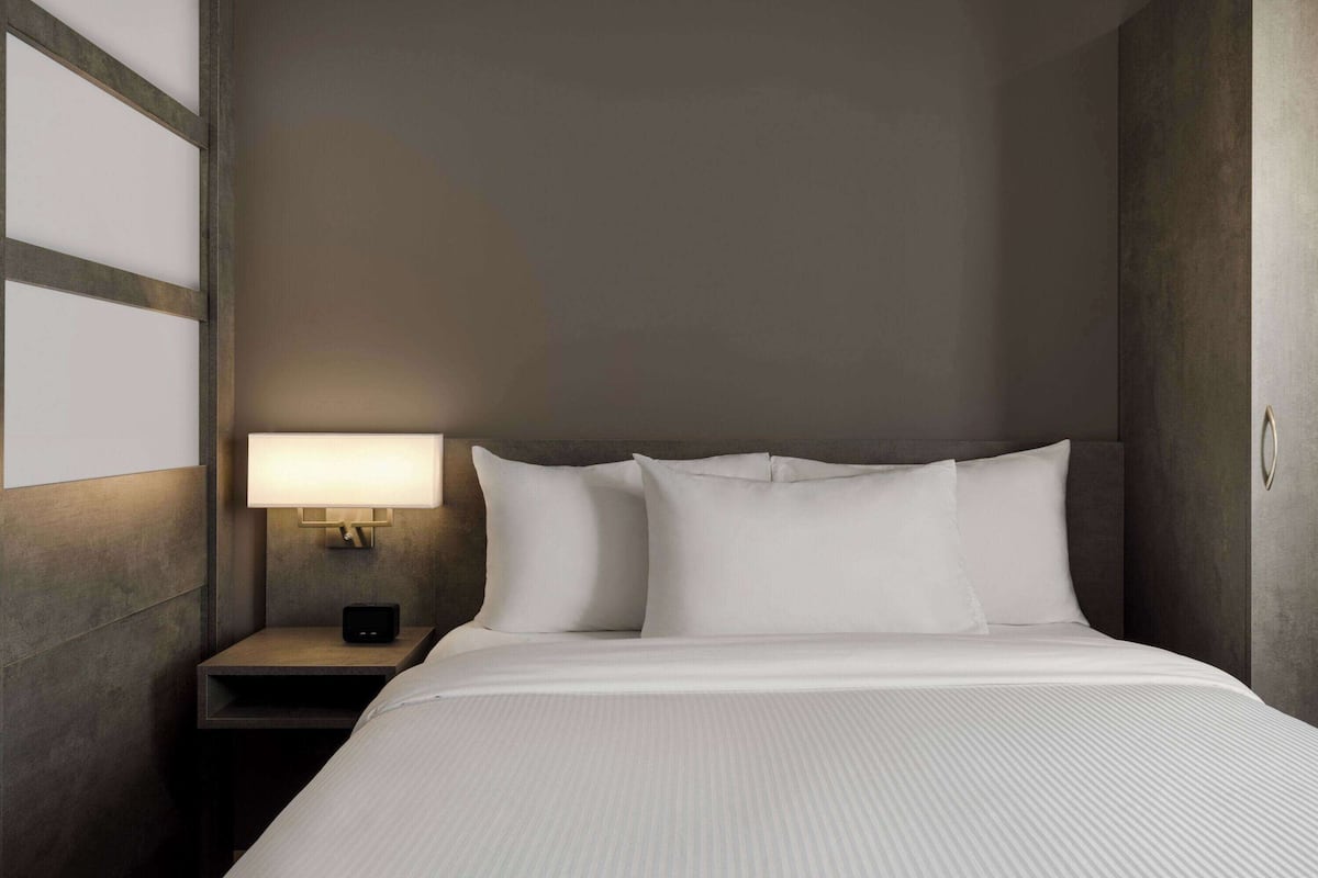 Un lit bien fait, avec du linge de lit blanc, dans une chambre d’hôtel.