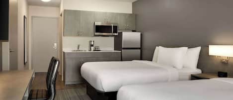 Habitación de hotel con dos camas, un escritorio, una silla, un microondas, un refrigerador y una pequeña kitchenette.