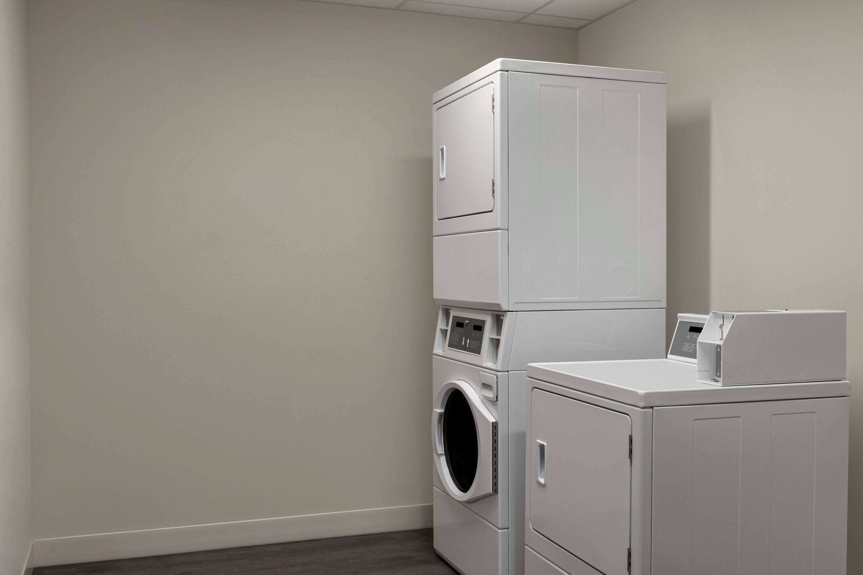 A laundry room with stacked washers and dryers, a control panel, and a small cabinet.