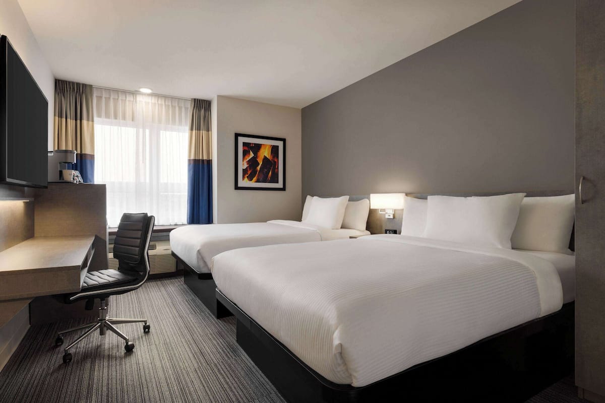 Une chambre d’hôtel avec deux lits, un bureau, une chaise, une télévision et un tableau au mur.