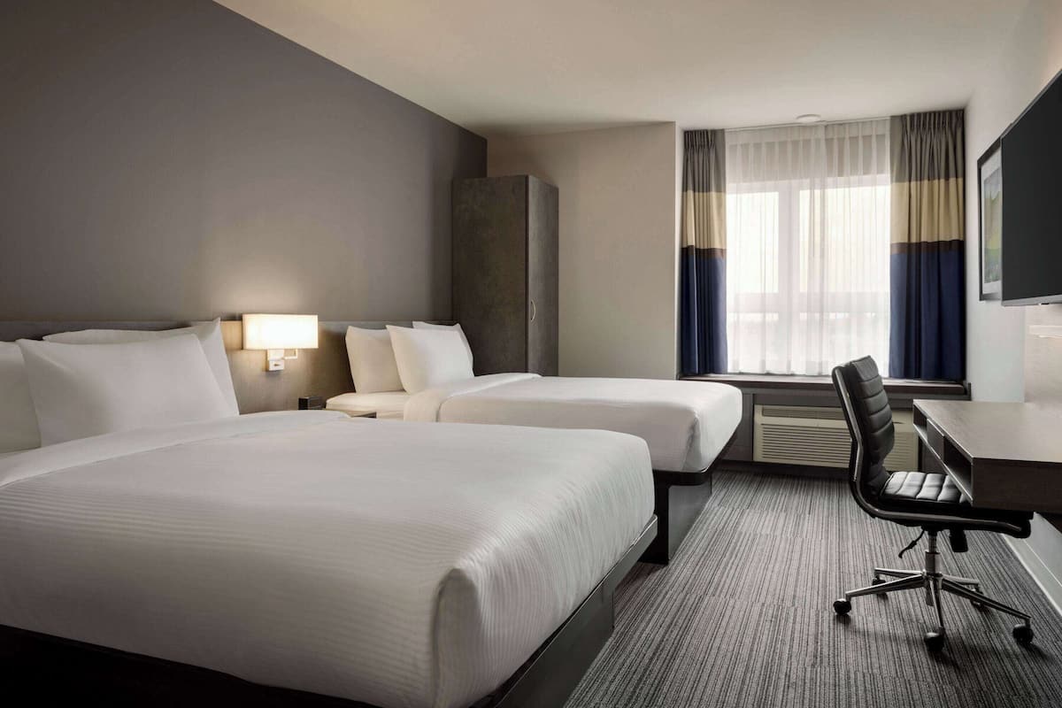 Une chambre d’hôtel avec deux lits, un bureau, une chaise, une télévision et une fenêtre avec des rideaux.