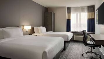 Een hotelkamer met twee bedden, een bureau, een stoel, een televisie en een raam met gordijnen.