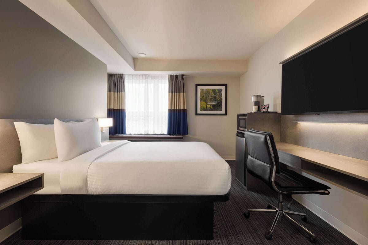 Une chambre d’hôtel avec un grand lit, un bureau, une chaise, un téléviseur à écran plat et une fenêtre avec des rideaux.