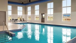 Une piscine intérieure à l’eau d’un bleu limpide, dotée de grandes fenêtres et offrant une vue sur l’extérieur.