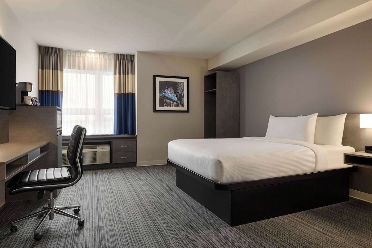 Une chambre d’hôtel avec un grand lit, un bureau avec une chaise, une télévision et une fenêtre avec des rideaux.