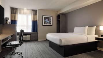 Habitación de hotel con una cama grande, un escritorio con silla, un televisor y una ventana con cortinas.