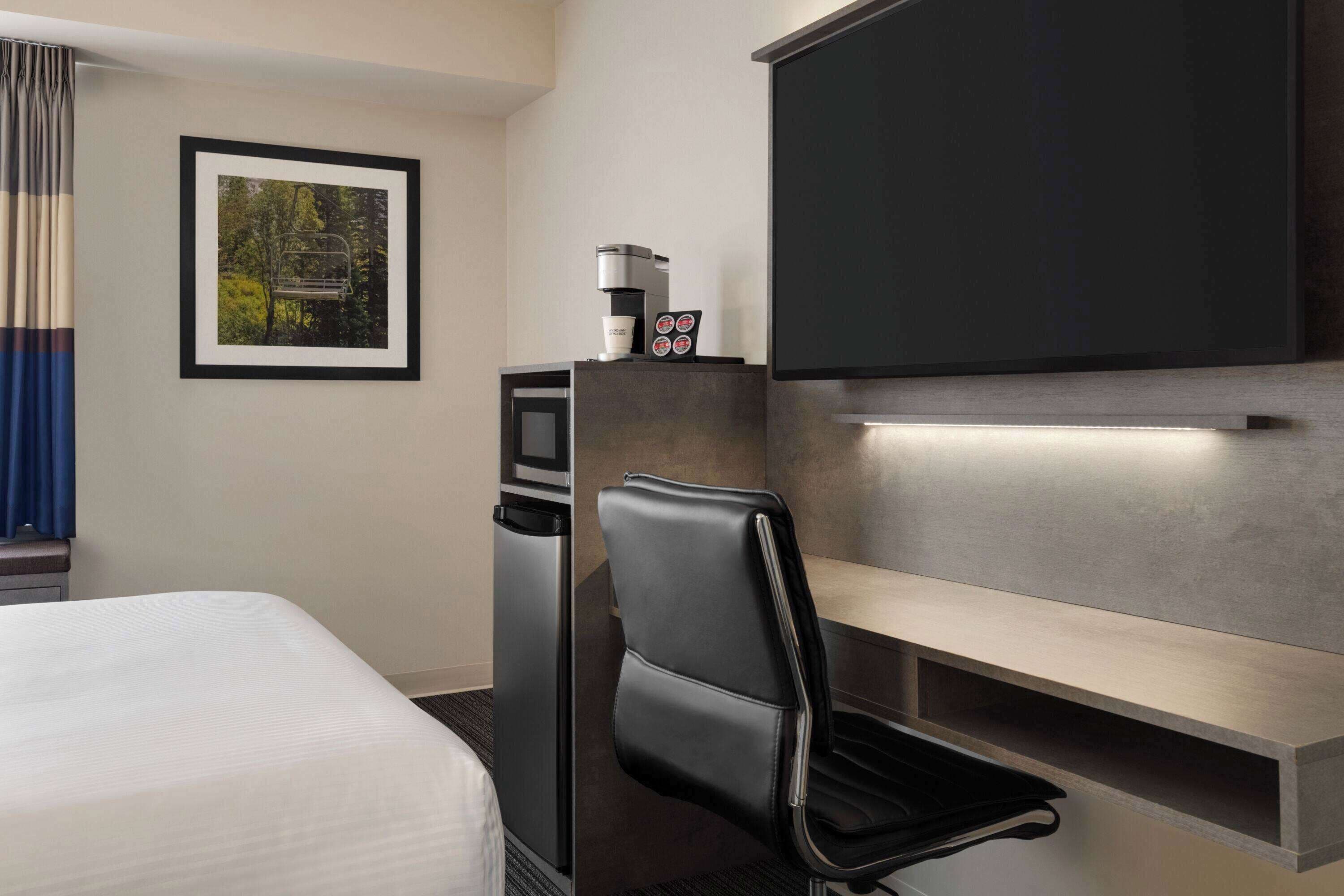 Una camera d'albergo con un letto, una scrivania con una macchina per il caffè, una sedia, un televisore e un quadro appeso al muro.