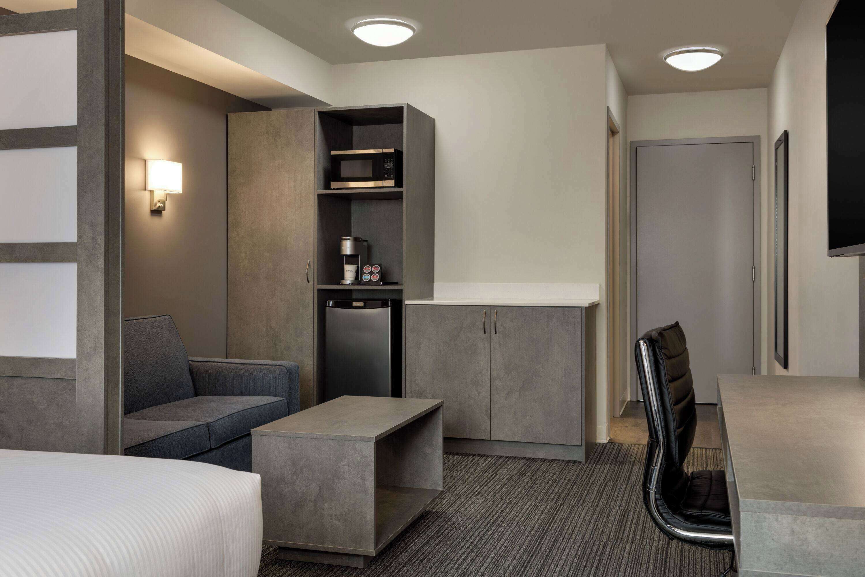Una habitación de hotel moderna con cama, sofá, escritorio, microondas y cafetera.
