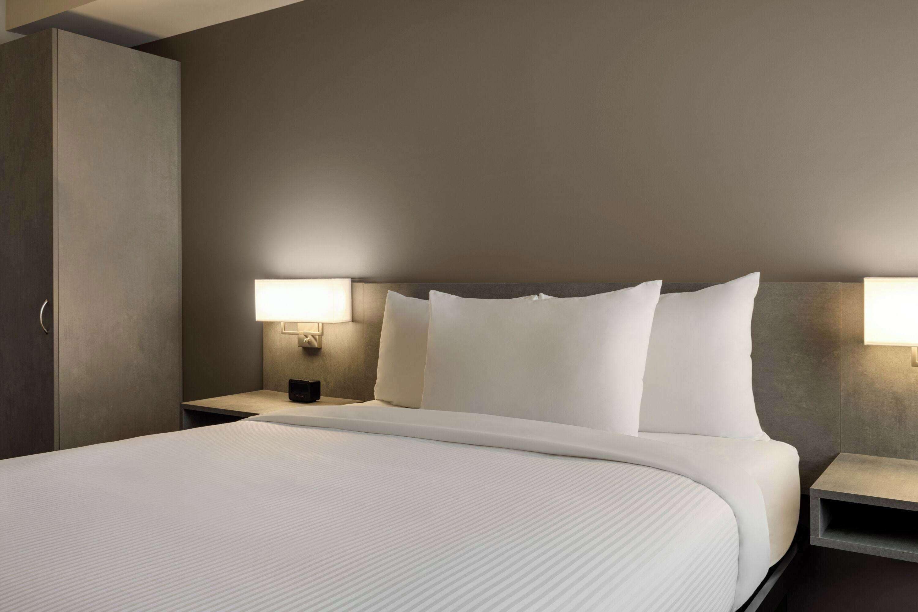 A modern hotel room with a large bed, two bedside tables, and wall-mounted lamps.