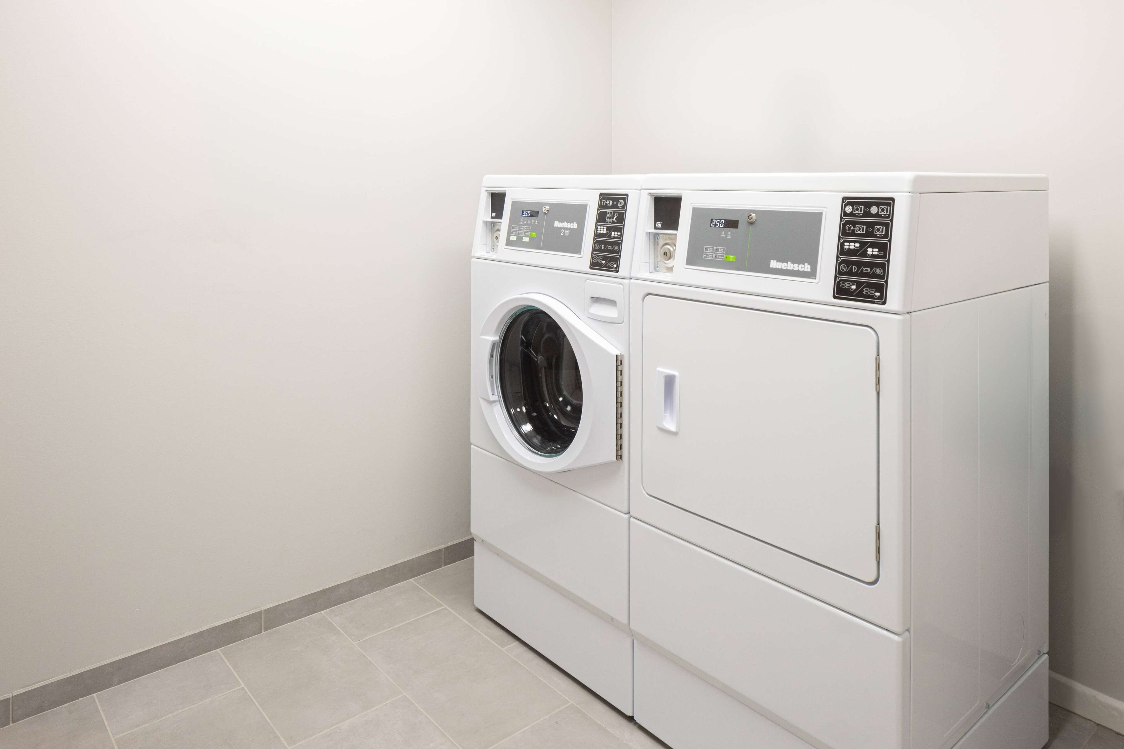 A compact, white, two-door washer and dryer unit with a digital control panel, located in a clean, tiled room with minimalistic decor.