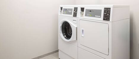 A compact, white, two-door washer and dryer unit with a digital control panel, located in a clean, tiled room with minimalistic decor.