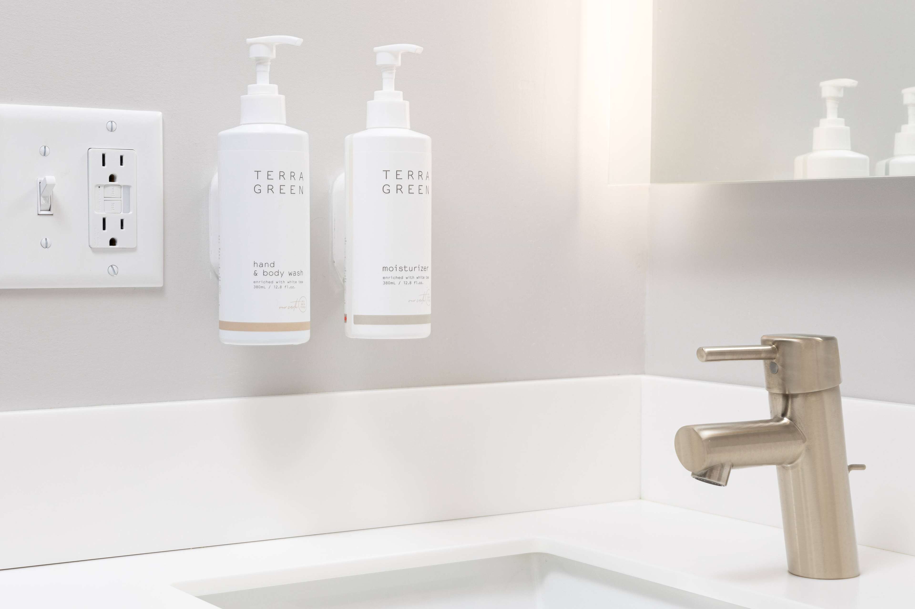 A modern bathroom with a white sink, a stainless steel faucet, and two bottles of Terra Green hand and body wash.