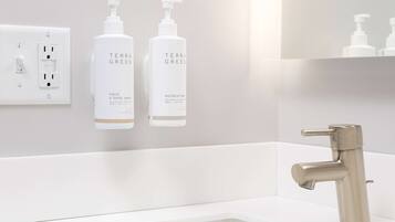 A modern bathroom with a white sink, a stainless steel faucet, and two bottles of Terra Green hand and body wash.