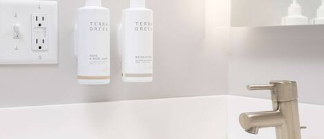 A modern bathroom with a white sink, a stainless steel faucet, and two bottles of Terra Green hand and body wash.