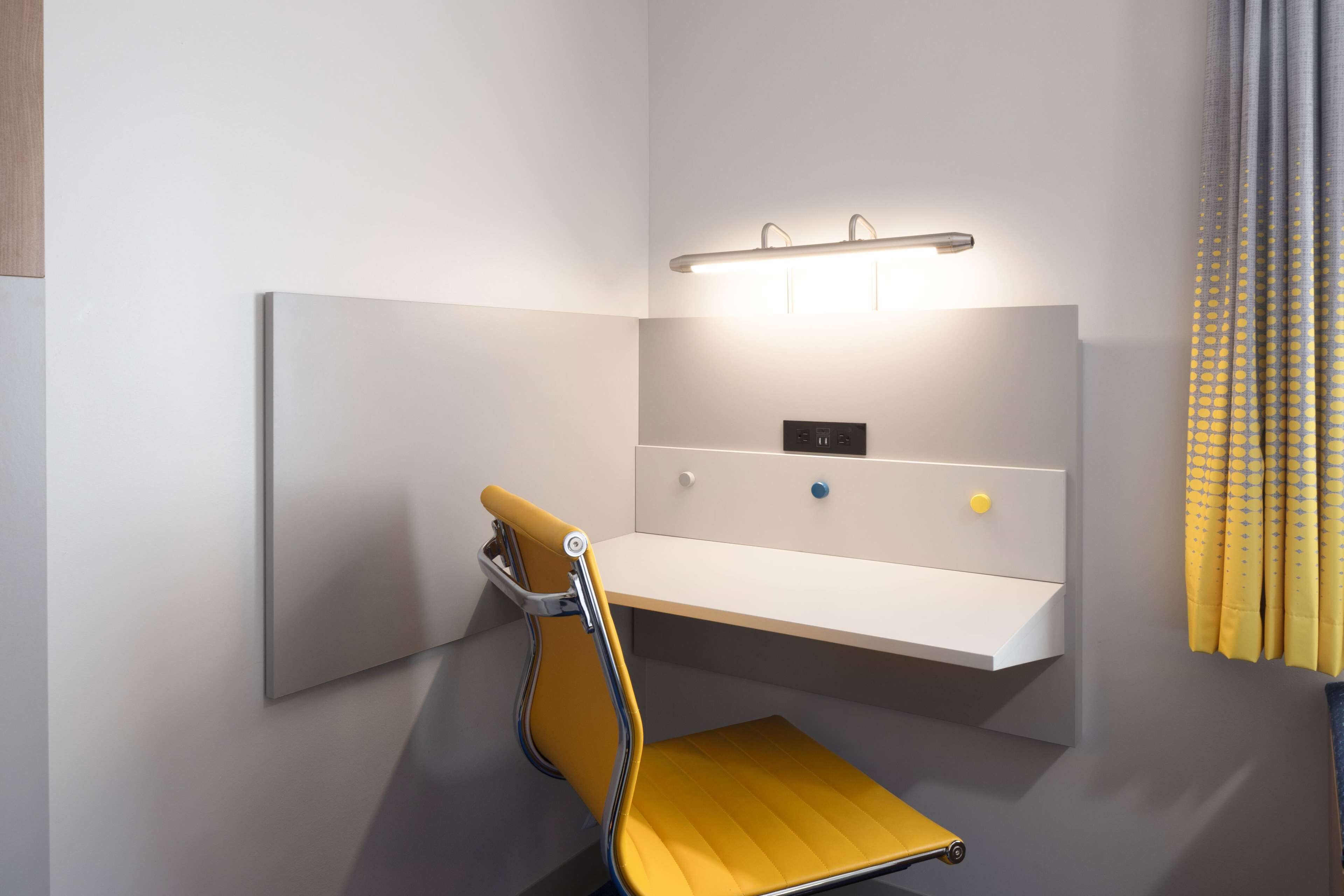 Une salle de bain moderne avec une chaise jaune, un meuble-lavabo blanc et un luminaire fixé au mur.