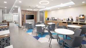 A modern dining area with round tables and chairs, a flat-screen TV, and a counter with various appliances.