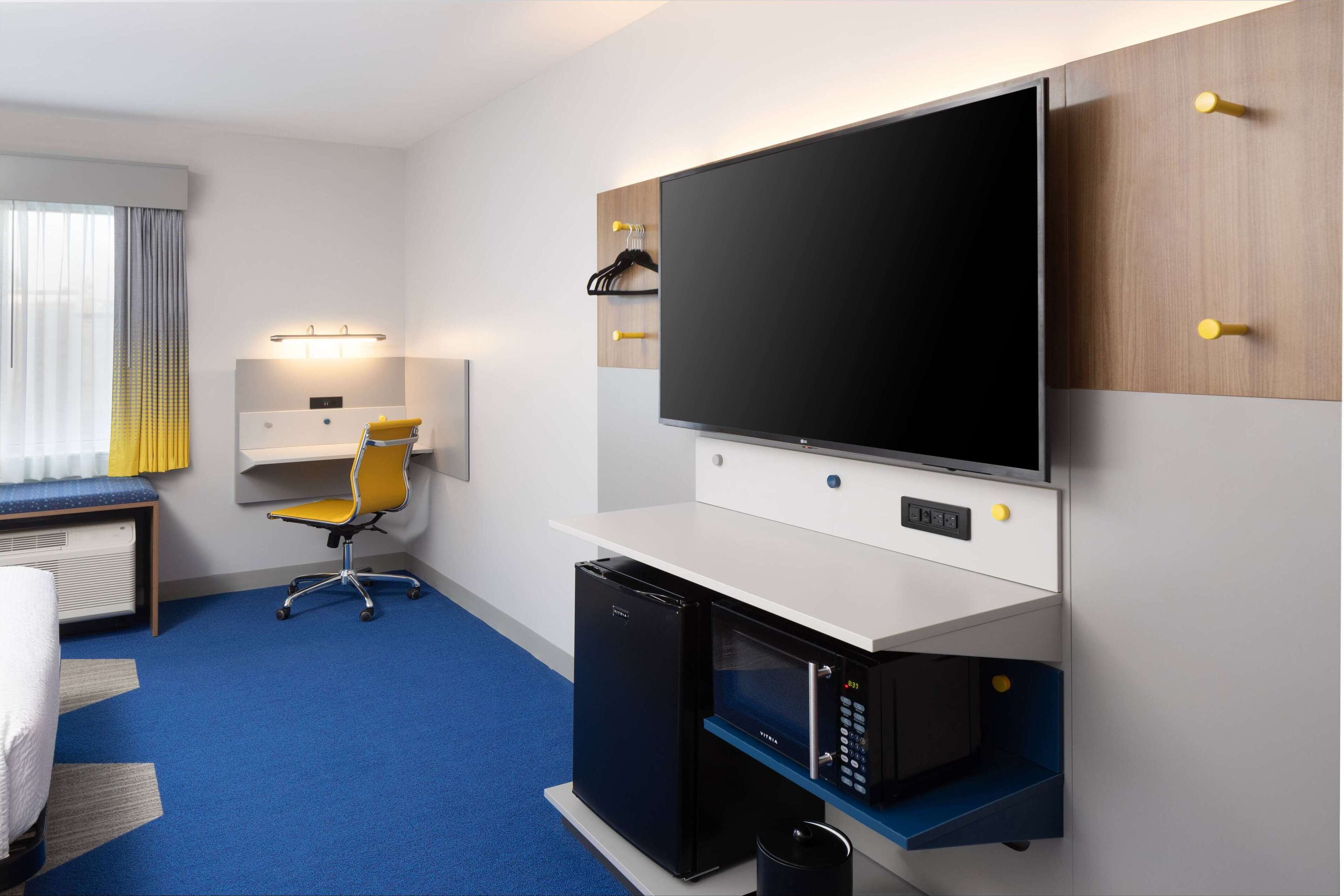 A hotel room with a bed, a desk with a chair, a television, a microwave, and a small refrigerator.