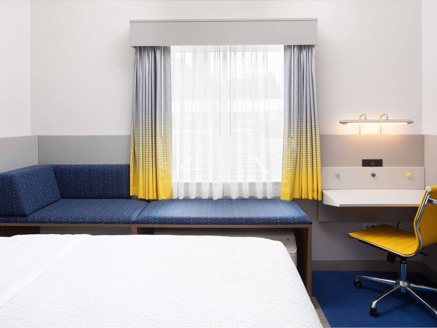 Une chambre d’hôtel avec un lit, un canapé bleu, un bureau avec une chaise et une fenêtre avec des rideaux.