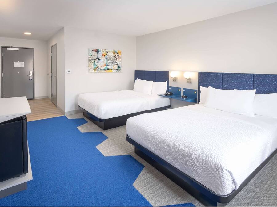 Quarto de hotel com duas camas, uma escrivaninha e uma obra de arte na parede.