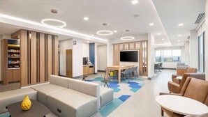 A modern hotel lobby with a sofa, a coffee table, a TV, and a dining area.