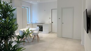 A modern kitchen with white cabinetry, a dining area with white chairs, and a large potted plant. - Fantastic Apartment in Historic Center - Palermo (Palermo)