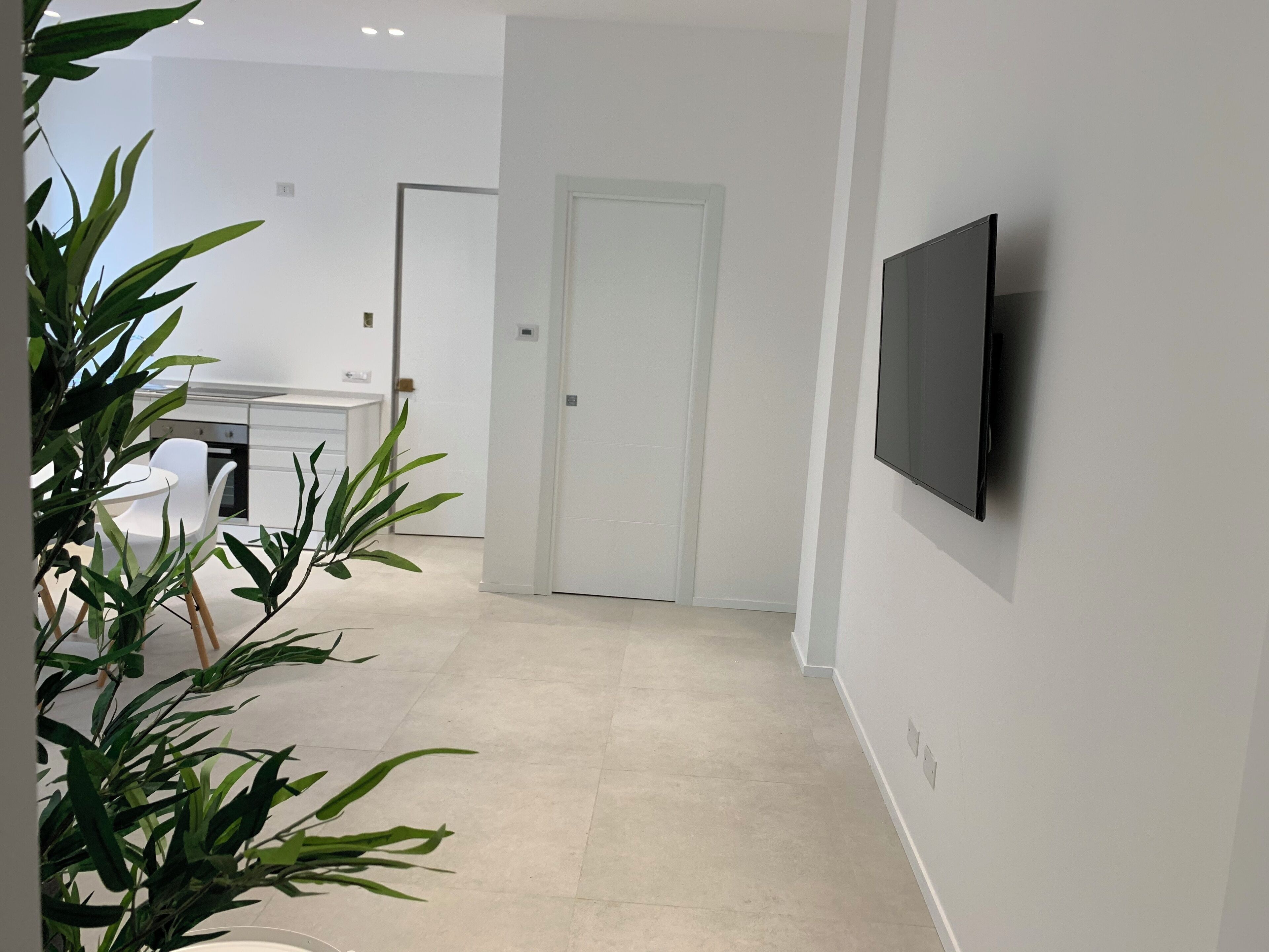 Una camera moderna e minimalista con una TV a schermo piatto montata a parete, una porta bianca e un piccolo tavolo con sedie.