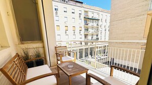 A balcony with a wooden table and two chairs, potted plants, and a view of adjacent buildings. - Fantastic Apartment in Historic Center - Palermo (Palermo)