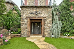 Un bâtiment en pierre avec une porte en bois, un chemin en pierre et un luminaire suspendu.
