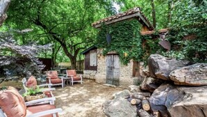 Un área de estar al aire libre rústica con paredes de piedra, mobiliario de madera y un hogar de piedra.