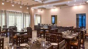 A hotel dining area with multiple tables and chairs, a bar counter, and ceiling fans. - MAULIK RETREAT (Ramnagar)