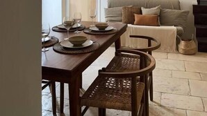 Un coin repas avec une table en bois dressée pour quatre personnes, une chaise en osier et un luminaire suspendu.