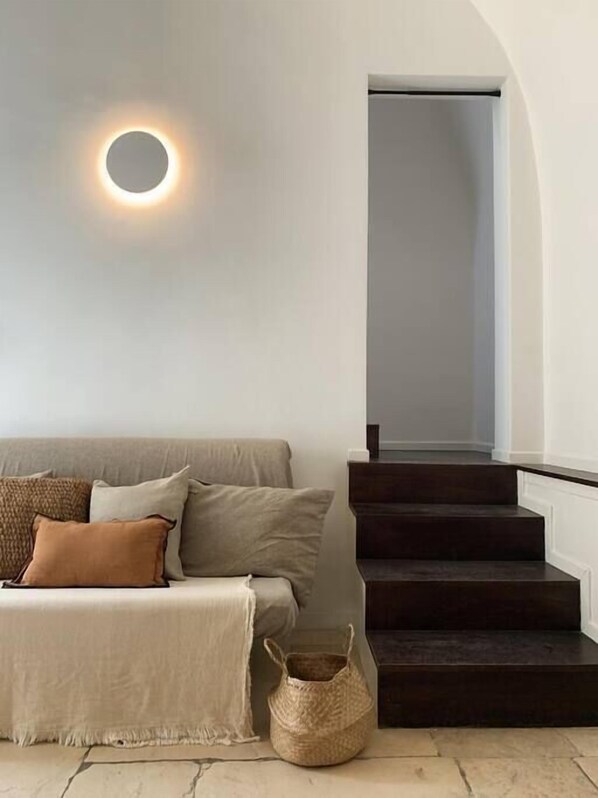 A modern living room with a sofa, a round wall light, and a staircase.