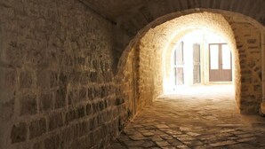 Un couloir en pierre, avec une porte en arc donnant sur une pièce dotée d’une fenêtre et d’une porte.