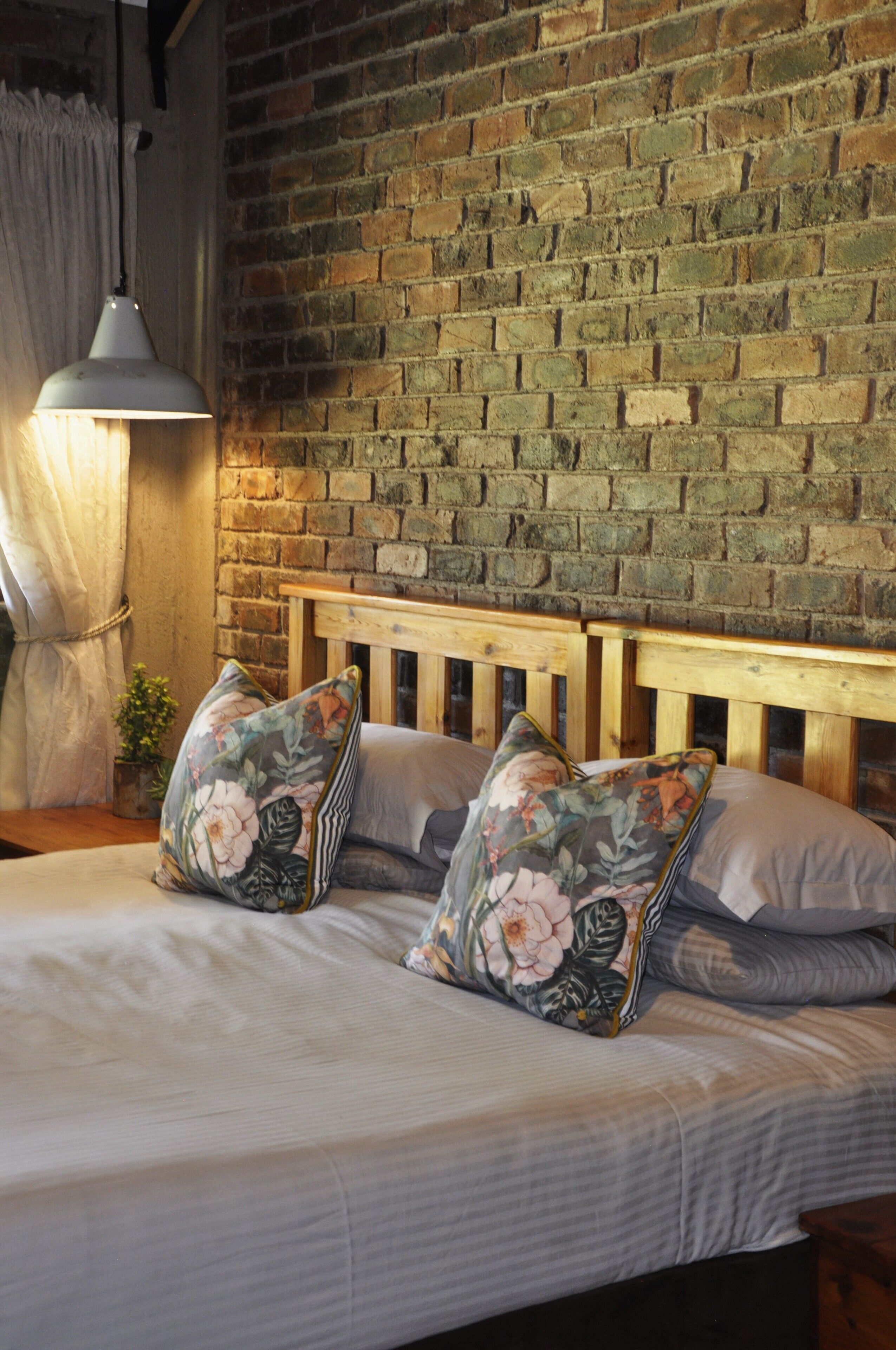 Una cama con almohadas estampadas, cabecera de madera y pared de ladrillo al fondo.