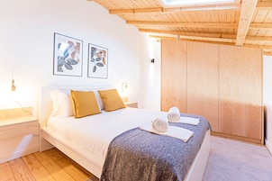A bedroom with a large bed, wooden headboard, two framed pictures on the wall, and a wooden wardrobe.