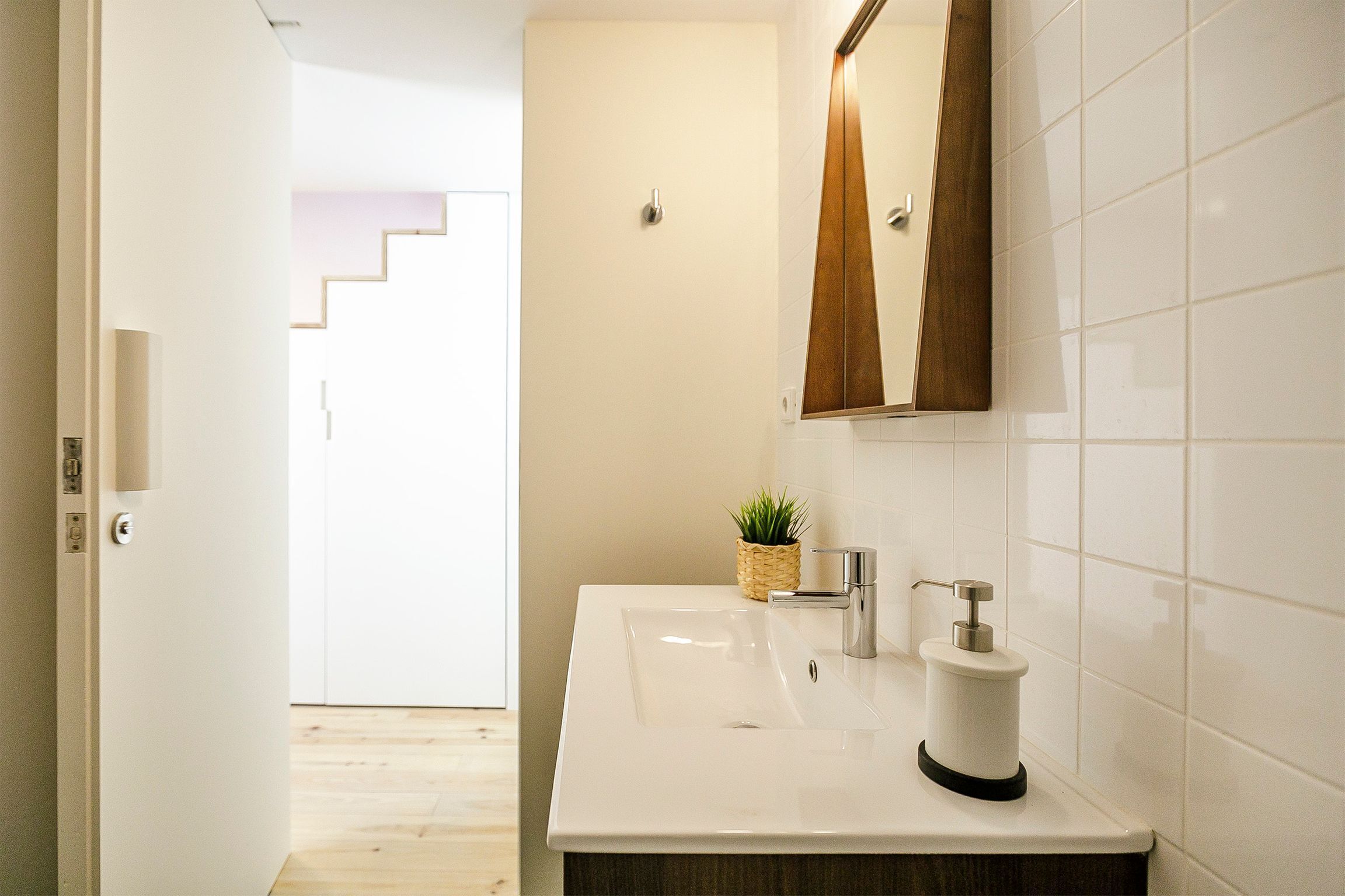 A bathroom with a white sink, a wooden-framed mirror, and a small plant on the counter.