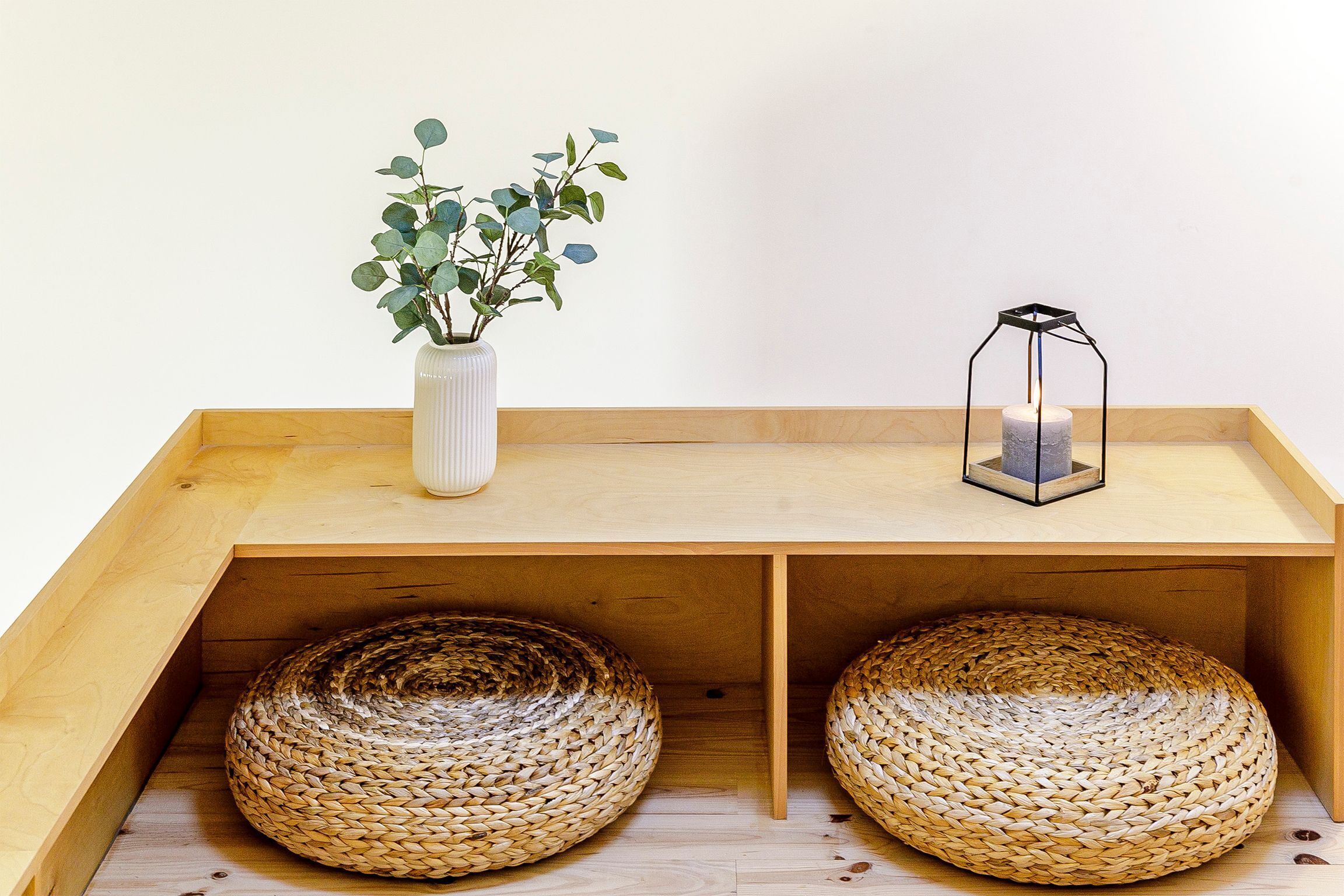 Un banc en bois, avec des paniers tressés placés en dessous, et une petite plante dans un vase blanc posé sur le banc.
