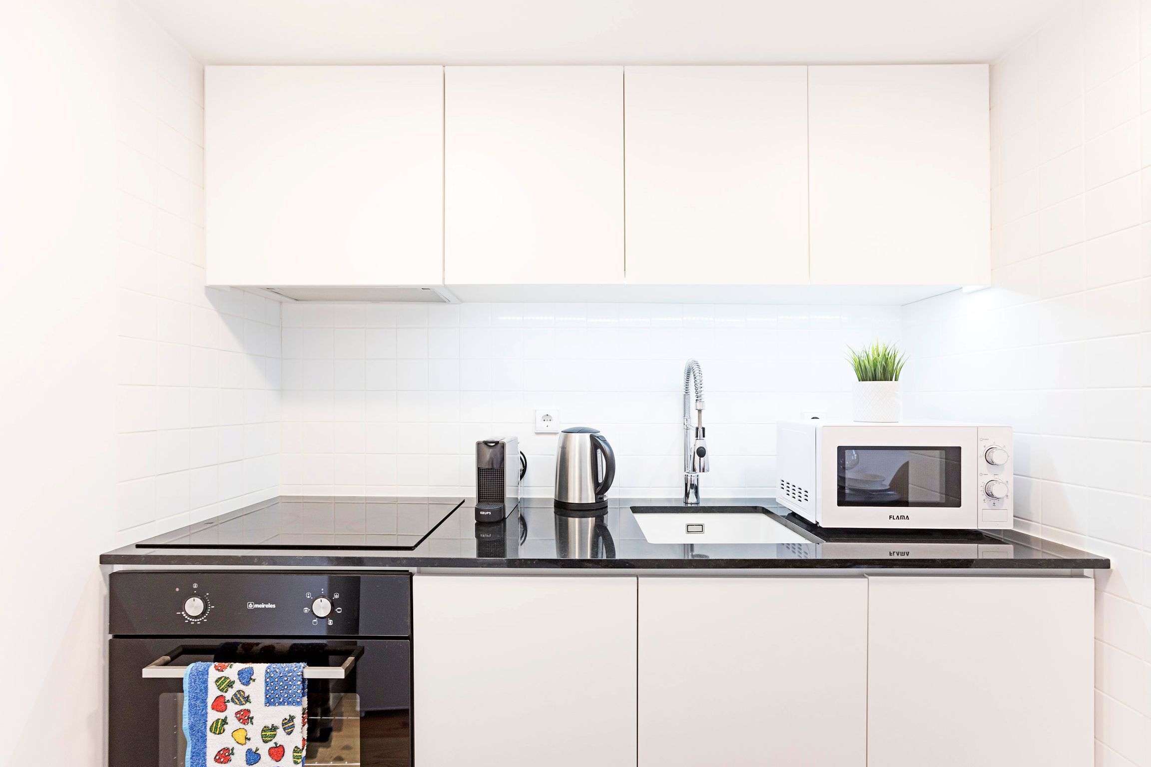 A modern kitchen with white cabinets, a black countertop, a microwave, a kettle, and a coffee maker.